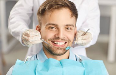 Klinikteki dişçiye giderken diş muayenesinden geçen bir adamın portresi. Doktor hastanın ağız boşluğunu incelemek için dişçilik aleti kullanıyor..