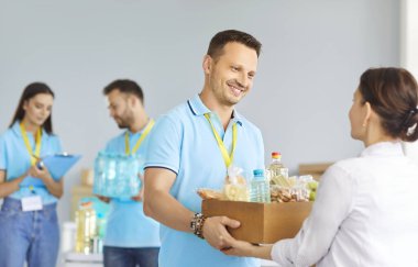 Mülteci bir kadına insani yardım merkezinde yiyecek bağış kutusu vererek yardım eden olumlu bir erkek gönüllü. Etkileşim, hayır kurumunun ve kamu hizmeti yardımının önemini vurguluyor.