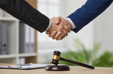 Profesyonel avukat ya da hukuk danışmanı bir müşteriyle tokalaşıyor. Takım elbiseli iki adam bir ofis masasında yargıç tokmağı ile tokalaşıyor. Erkek ellerine yakın çekim. Hukuk, hukuk hizmetleri kavramı