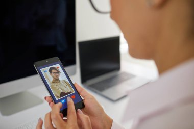 Aşkı ara. Genç bir kadının cep telefonundaki flört uygulamalarındaki erkeklerin profillerine göz atmasına yakın çekim. Kadın ekranda beliren adamın sempatisini kazanmak için kırmızı bir kalbe basmak üzere..