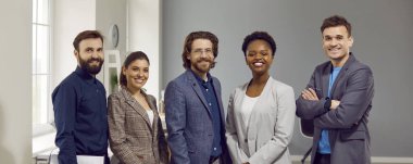 İşteki mutlu iş adamlarının portresi. Takım elbiseli beş başarılı beyaz ve Afrikalı Amerikalı ofiste kameraya bakıp gülümsüyor. Sancak, başlık arkaplanı