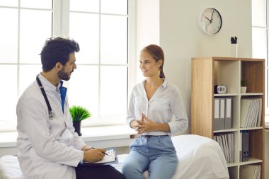 Erkek doktor ya da pratisyen hekim modern hastanedeki gülümseyen kadın hastalara danışıyor. Erkek terapist klinikteki kadınla düzenli olarak görüşüyor. Sağlık, tıp, iyi hizmet kavramı.