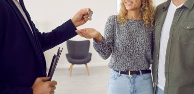 Emlakçı, evli çiftlere evin anahtarlarını verir. Yeni dairenin oturma odasında duran ve emlakçının onlara verdiği anahtarları alan mutlu sevgili ve sevgili ya da karı-koca pankartı.