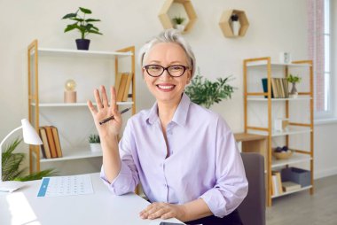 Video konferansı sırasında el sallayan olgun orta yaşlı bayan öğretmen sanal web kameralı sohbet için arıyor. Gülümseyen kadın uzak mesafeden öğrencileriyle buluşuyor. Web kamerası görünümü.