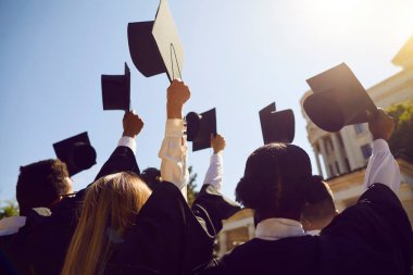 Eğitimi bitiren öğrenciler mezuniyet gününde şapkalarını havaya kaldırırlar. Prestijli üniversitenin kendine güvenen mezunları güneş ışığında parlak mavi gökyüzüne kadar kare akademik şapkalarla el kaldırsın.