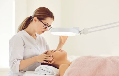 Kadın dermatolog modern güzellik kliniğindeki müşteriler için cilt bakımı prosedürü uyguluyor. İlgili kozmetik uzmanı estetik tıp salonundaki kadın hastalara yüz gerdirme tedavisi uyguluyor. Kozmetoloji kavramı.
