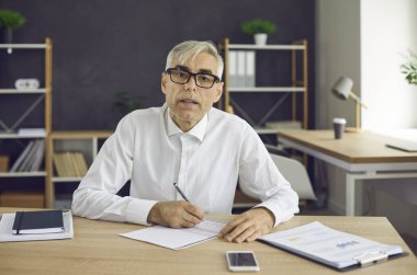 Odaklanmış iş adamları not alır ve kendileri için önemli bilgiler yazarlar. Adam masaya oturur ve kameraya bakar. Sanki önünde oturan adamı dikkatle dinlermiş gibi..