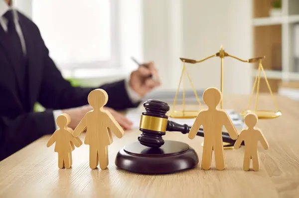 Gavel, ses bloğu ve arka planda adalet terazisi ve yargılanması için mahkeme masasına bırakılan aile ve çocukların tahta figürleri. Aile hukuku, mahkeme, boşanma, çocuk velayeti kavramı