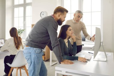 Üç kişilik bir grup bilgisayar ekranına bakıyor ve bir şeyi tartışıyor. Genç ve yaşlı şirket çalışanlarından oluşan bir ekip modern ışık şirketinin iç işlerinde online proje üzerinde çalışıyor.