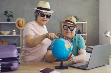 Mutlu emekli çift birlikte tatil yapmayı planlıyor. Şapkalı ve güneş gözlüklü neşeli yaşlı insanlar Dünya 'daki hedeflerini seçiyorlar. Seyahat ve aktif tatil kavramı