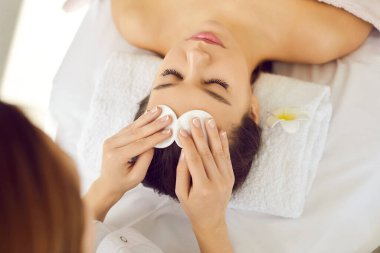 Modern spa salonunda ya da güzellik merkezinde güzellik uzmanları kadın makyajını pamuk disklerle temizliyor. Yüz masajı, kimyasal cilt bakımı ya da detoks maskesi gibi yüz masajından önce.