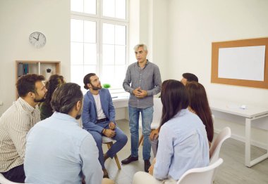 Ofiste ciddi bir iş görüşmesi yapan bir grup insan. Kıdemli adam iş arkadaşlarıyla konuşurken ayağa kalkar. Şirket lideri, çalışanlara danışmanlık ve danışmanlık hizmeti sunar