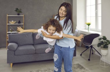 Mutlu bir aile evde harika vakit geçiriyor. Anne ve çocuk birlikte eğlenceli oyunlar oynuyorlar. Gülümseyen, gülen ve uçan bir uçakmış gibi davranan küçük tatlı kızını taşıyan neşeli bir anne.