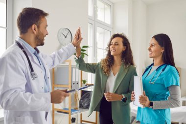 Tedavi başarılı olduğu için sevinen hemşire dostu doktor muayene sonrası klinikte ayakta duran gülümseyen kadın hastaya beşlik çakıyor. Sağlık ve Tıp Konsepti.