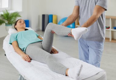 Fizyoterapist hasta bacağı yaralanması ya da ağrı kesiciler üzerinde çalışıyor. Erkek terapist, kadın müşteriyle egzersiz yapar. Hızlı iyileşme için rehabilitasyon uygular. Rehabilitasyon ve fizyoterapi.