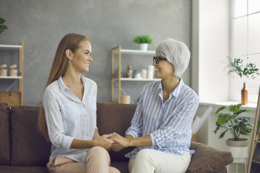 Yaşlı anneyi sevmek, yetişkin kızıyla vakit geçirmek. İki farklı nesilden iki güzel kadın bir aile evlerinde kanepede oturuyor, birbirlerine bakıyor, el ele tutuşuyor ve gülümsüyorlar.