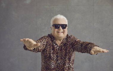 Komik, zengin, tombul bir emekli aktif fitness egzersizi yapıyor. Stüdyo portresi. Beyaz saçlı, şişman, leopar gömlekli ve güneş gözlüklü spor yapan son sınıf öğrencisinin.