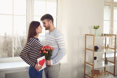 Sevgililer Günü. Adam, odadaki kanepede oturan bir kıza kırmızı kalpli bir sevgililer günü kartı veriyor..