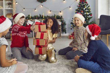 Group of happy mixed race children sitting on floor and collecting heap of gift boxes at home party during Christmas or New year in decorated room. Children party of different nationalities clipart