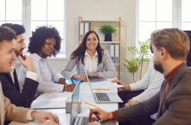 Mutlu farklı iş adamları ofis toplantısı hakkında olumlu konuşuyorlar, gülüyorlar, konferans masasında beyin fırtınası yapıyorlar, haberleri dinleyen kendine güvenen kadın konuşmacı, grup yönetim kurulu başkanı.