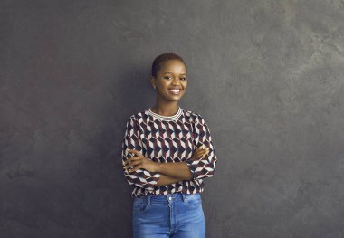 Olumlu duygular. Gri arka planda duran güzel gülümseyen Afrikalı Amerikalı kadının stüdyo portresi. Kısa saçlı, sıradan elbiseli genç bir kadın kameraya bakarak samimi bir şekilde gülümsüyor..