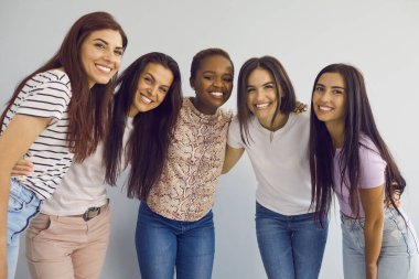 Uluslararası arkadaşlık. Beş genç kadının portresi. Yan yana duran ve kameraya gülümseyen. Hafif bir arka planda dururken içten bir şekilde gülümseyen ve sarılan bir grup mutlu kadın..