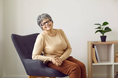 Gülümseyen olgun beyaz saçlı kadının portresi sandalyeye oturup mutlu olgunluğun tadını çıkarıyor. Gözlüklü mutlu yaşlı kadın evde ya da huzurevinde koltukta dinleniyor. Emeklilik ve emeklilik.