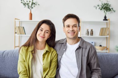 Evdeki mutlu genç çiftin portresi. Kameraya bak, yeni evdeki koltukta rahatla, gülümseyen koca, birlikte poz ver, iyi ilişkiler, ev sahipleri, ev sahiplerinin keyfine bak. 