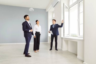 Pencereden manzaraya bakan genç ve mutlu bir çifte ev gösteren bir emlakçı. Profesyonel emlakçı yeni bir daire gösterdi. Aile ev sahibi olmaya hazır. Emlak piyasası kavramı.