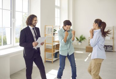 Neşeli, mutlu, mutlu bir aile çifti yeni bir apartman dairesi almaktan mutlu genç bir emlakçıyla birlikte emlak satın almaktan keyif alıyorlar. Taşınma günü konsepti.