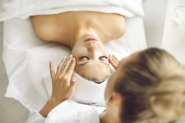 Güzellik uzmanı ya da kozmetikçi, güzellik salonundaki kırışıklık önleyici kozmetik işlemleri için genç kadın yüzüne nemlendirici çarşaf maskesi uyguluyor. Kozmetoloji ve profesyonel cilt bakımı kavramı.