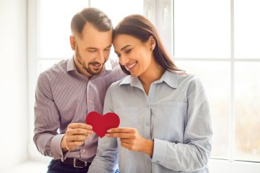 Neşeli gülümseyen genç bir çiftin portresi. Kırmızı kalbi içeride tutan erkek ve kadın. Sevgilisine aşık olan mutlu bir erkek. Sevgililer Günü, şefkat ve ilgi konsepti.