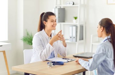 Klinikte muayene sırasında hasta kadınla konuşan gülümseyen genç bir kadın doktorun portresi. Sağlık ve Tıp Konsepti.