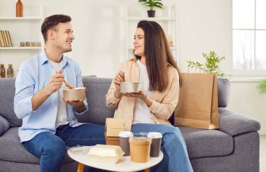 Genç ve mutlu bir çift evdeki oturma odasındaki kutularda yemek yiyip sohbet ediyorlar. Birlikte yemek yiyorlar. Aile yanında hazır yiyecek ve içeceklerle oturuyor. Teslimat hizmeti kavramı.