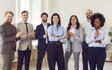 Çok ırklı mutlu birleşmiş takımın grup portresi yeni iş arkadaşını alkışlıyor, başarılı çalışanları iş yerinde bir araya getiriyor ve kameraya gülümseyen iş arkadaşlarını selamlıyor. 