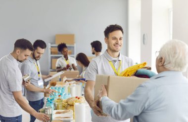 İnsani yardım merkezindeki yaşlı bir adama yiyecek kutusu vererek gönüllü olarak yardım sağlıyorsun. Sadaka ve bağış, ihtiyacı olanlara yardım ve destek sunmaya adanmışlığı ön plana çıkarıyor.