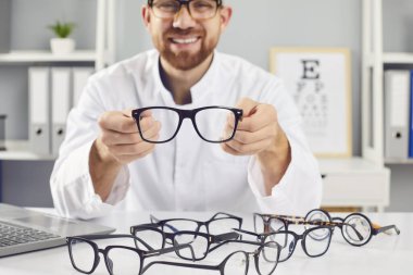Gözlük gösteren oftalmolog, klinikte gülümseyen doktor, doğru tıbbi görüş hizmetini seçmeye yardım ediyor. Optik mağazada optometri problemleri, göz testleri, kontak lenslerin reçetelendirilmesi 