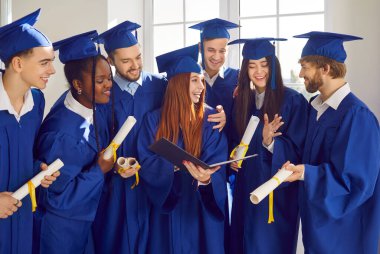 Gülümseyen mutlu uluslararası mezun öğrencilerin portresi üniversite mezuniyet elbisesi içinde konuşuyor ve eğleniyor ve içeride diploma tutuyor. Eğitim ve mezuniyet kavramı.