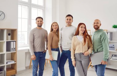 Bir grup genç kadın ve erkek kameraya bakıyor ve ofiste gülümsüyor. Çalışanların takımı, şirket çalışanları ya da bir grup öğrencinin güvenli ve neşeli bir şekilde sıraya girmesi..