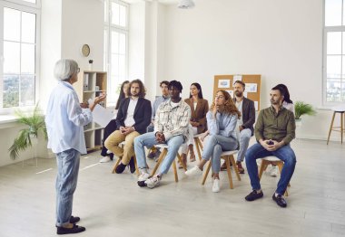 Çeşitli iş adamlarından oluşan bir grup, iş projesini görüşmek için ofiste sırayla oturuyorlar. Şirket çalışanları konferans odasında olgun bayan meslektaşlarını dinliyorlar..