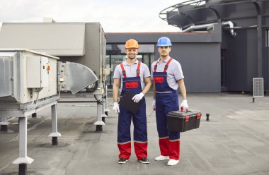 Çatıdaki iklim sistemlerine hizmet eden işçiler ya da mühendislerin portresi. Bakım, onarım ve servis işleriyle uğraşan bu teknisyenler binanın HVAC sisteminin çalışmasını sağlıyorlar..