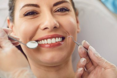 Hastanedeki dişçi randevusuna geniş gülümsemeli bir hastanın portresi, diş aletini kullanarak diş kontrolü yapan bir doktor. Düzenli diş muayenesi ve oral bakım..