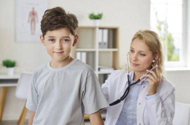 Mutlu okul çocuğu klinikte bir doktor tarafından muayene ediliyor, yakın plan. Klinikteki çocuk doktoru bir gencin akciğer sağlığını kontrol ediyor. Konsept doktor muayene odası, sağlıklı refah, dostça söyle