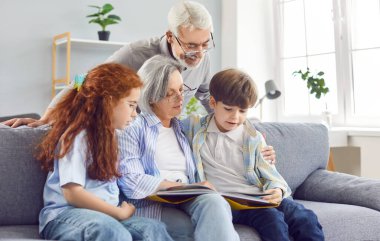 Büyükannem torunlarına evde kanepede kitap okuyor, yakın plan. Büyükbaba ve büyükanne torunlara okumayı öğretiyor. Kavram birlikte eğlenmek, iyi ilişkiler, büyükanne ve büyükbaba