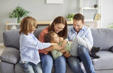 Aile eğlencesi, heyecanlı ebeveynler sevgili küçük kızı gıdıklıyor, evde çocukla oynuyor neşe içinde gülüyor, aile sevgisinin tadını çıkarıyor, olumlu ilişki yaşıyor, haftasonu neşeli anları, boş zaman aktiviteleri...