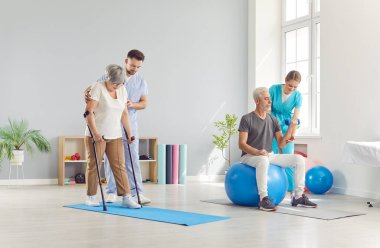 Rehabilitasyon kliniğinde spor yapan yetişkin insanlar ya da sağlık görevlilerinin yardımıyla egzersiz yapıyorlar. Fizyoterapistle beden eğitimi için egzersiz yapan emekli adam ve kadın.