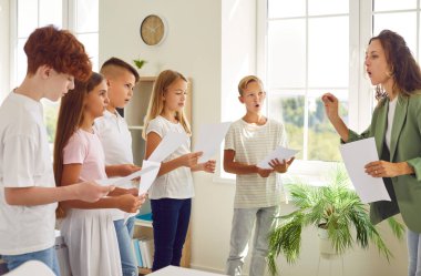 Öğretmen ve bir grup öğrenci bir müzik dersi sırasında bir okul sınıfında birlikte şarkı söylüyorlar. Müzik, öğrenme ve uyum içinde olma sevinci içinde oldukları için atmosfer canlı..