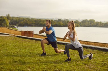 Aktif genç çift doğada esneme egzersizi yapıyor. Spor giyim kuşamında mutlu bir kadın ve erkek parkta spor yapıyor. Açık hava eğitimi ve spor konsepti.
