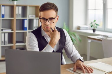 İşadamı büroda çalışıyor, dizüstü izliyor, düşünüyor, düşünüyor. Genç çalışan çalışmakla meşgul, bilişim sektörü analisti stratejik çözümü anlıyor, teknolojik çözüm buluyor, müşteriye yardım ediyor