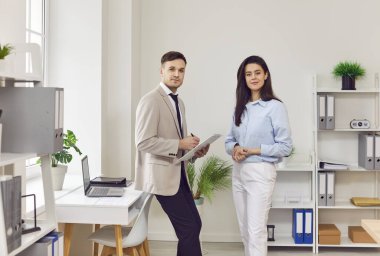 Genç erkek, kadın çalışanlar modern ofis çalışma alanında duruyor, iş adamları ortak odada çalışıyor, yeni stajyer arkadaşlara öğretmenlik yapıyor, takım çalışması şirket rehberliği yapıyor.